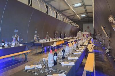 Salle lumineuse avec tables dressées pour un repas, chaises rouges, lampes suspendues et personnes en arrière-plan.