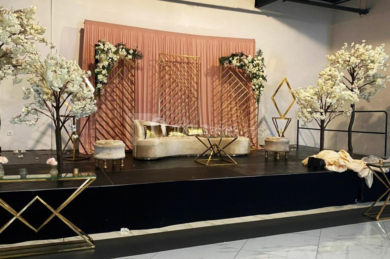 Scène décorée avec des fleurs blanches, un canapé beige, des coussins dorés et des tables en métal doré.