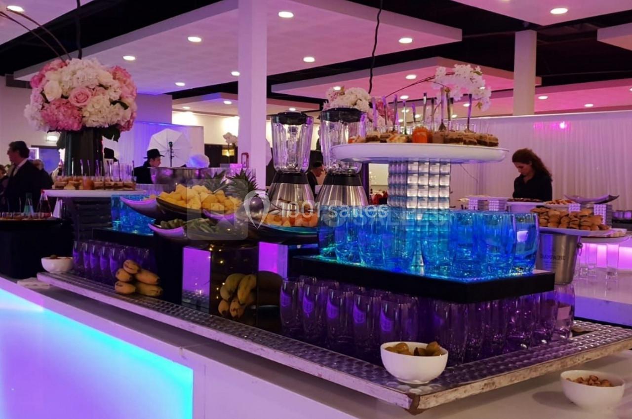 Buffet élégant avec verrerie, fruits, fleurs et éclairage coloré dans une salle de réception moderne.