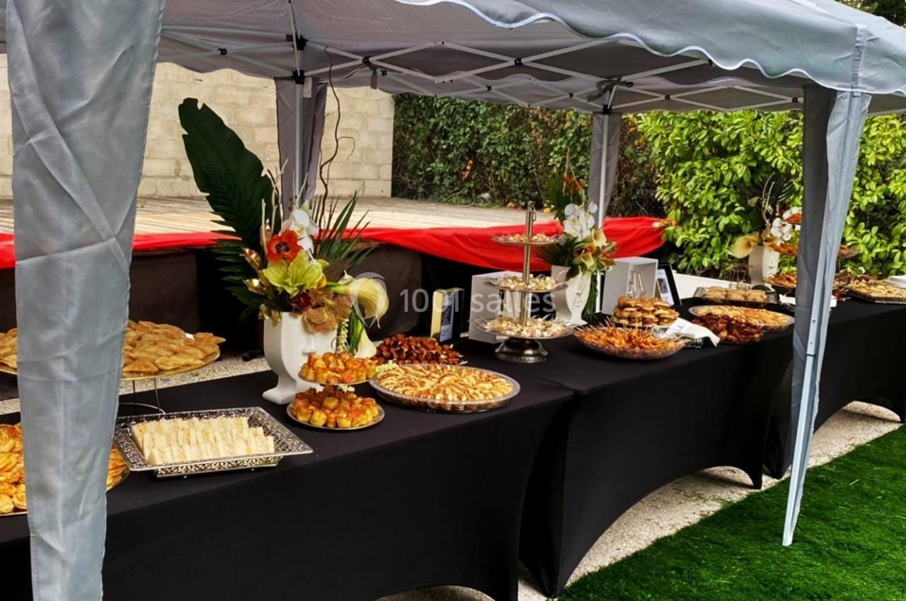 Buffet en plein air sous une tente, avec des tables noires garnies de plats variés et de décorations florales.