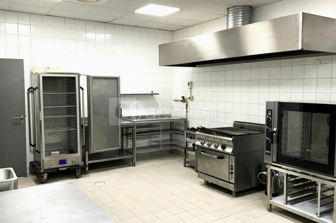 Cuisine professionnelle équipée avec four, réfrigérateur, plan de travail en inox et hotte d'extraction.
