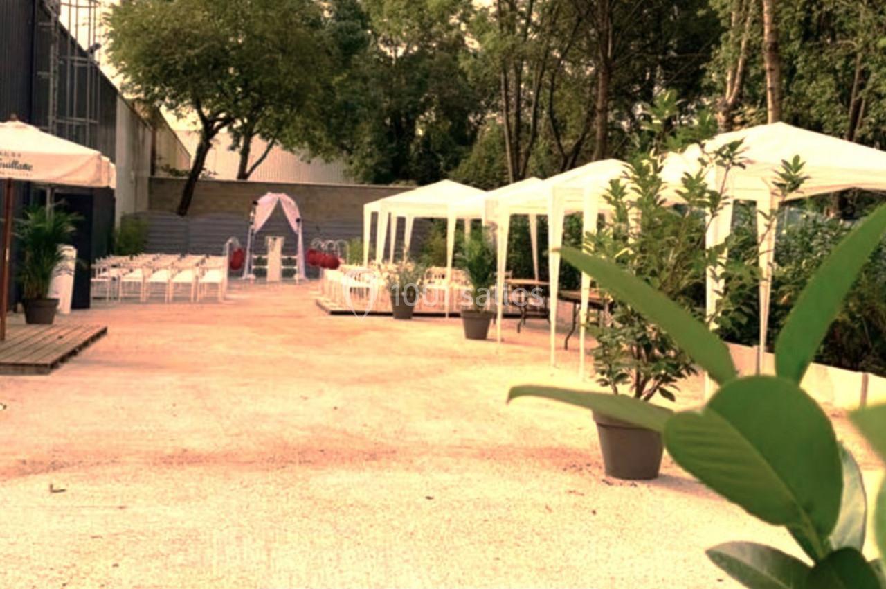 Espace extérieur aménagé avec des tentes blanches, des chaises alignées et des plantes, entouré de verdure.