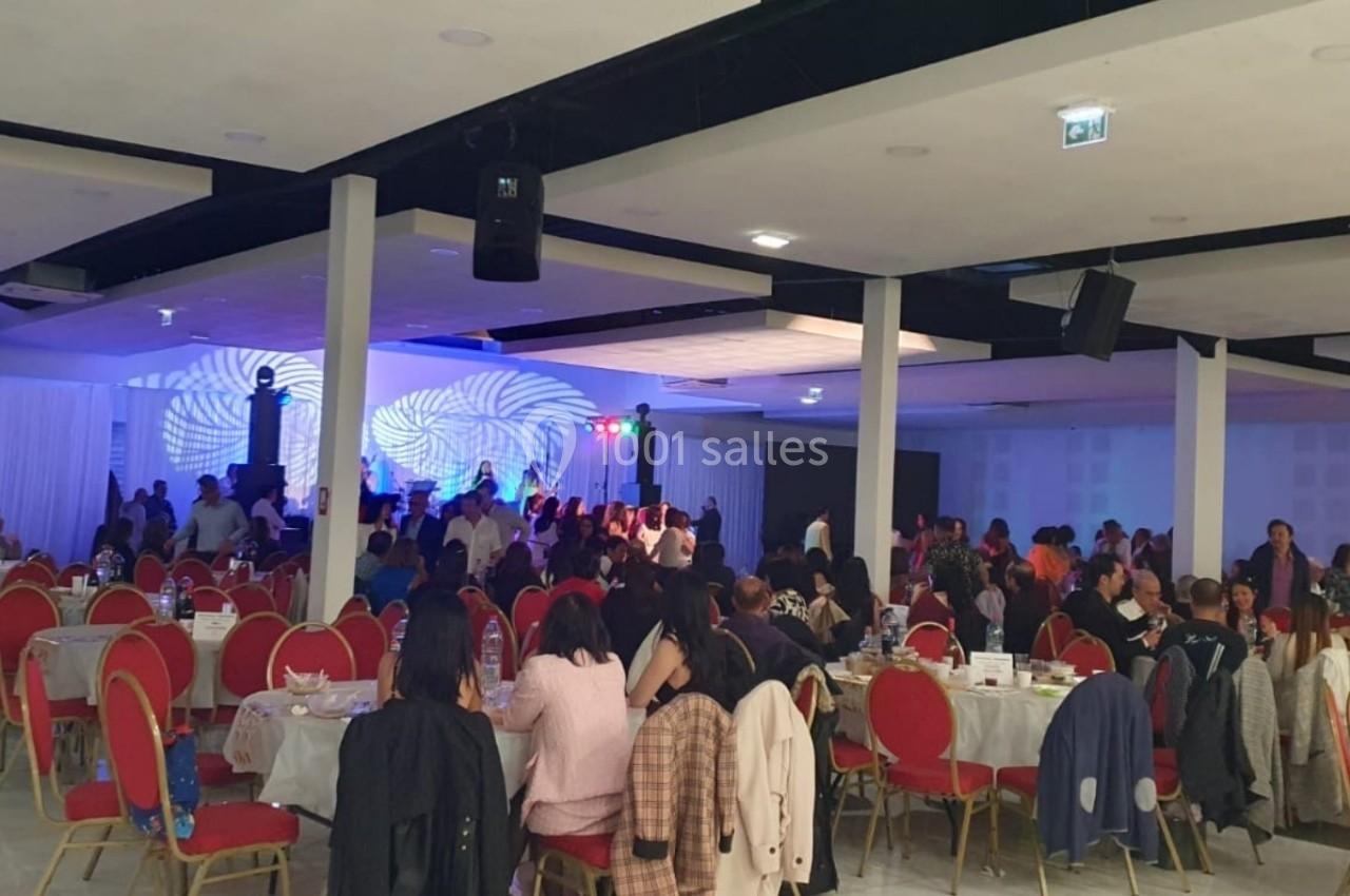 Salle de réception avec des invités assis à des tables rondes et une scène éclairée en arrière-plan.