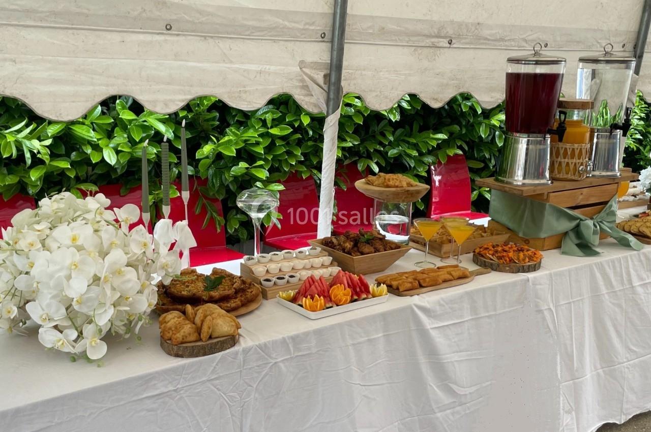 Buffet sous une tente avec viennoiseries, fruits, plats salés et boissons disposés sur une table blanche.