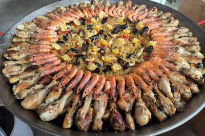 Salle lumineuse avec poutres apparentes, tables rondes dressées avec nappes blanches et chaises en plastique blanc.