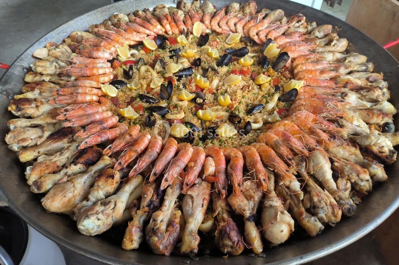 Grande paella garnie de crevettes, moules, morceaux de poulet et légumes colorés, présentée dans une large poêle.