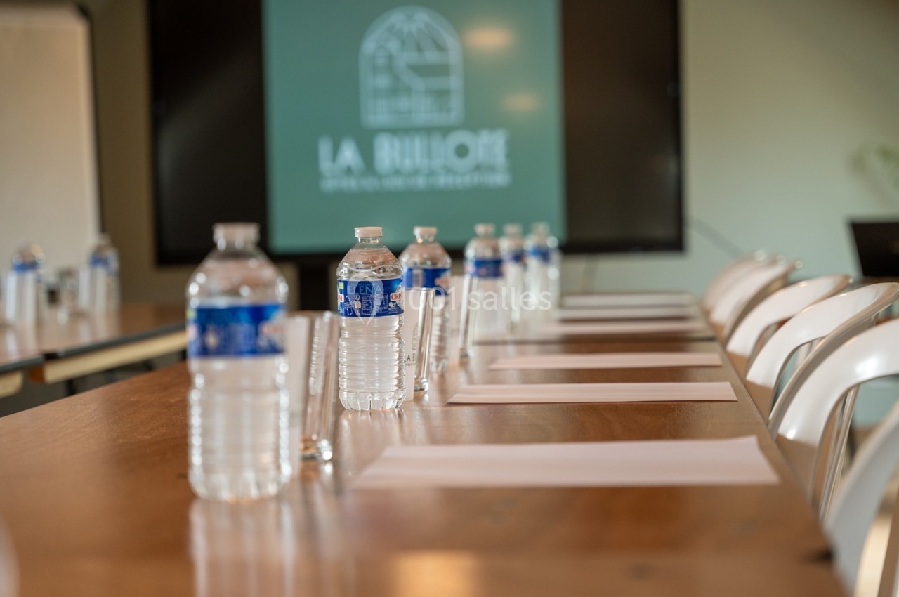 Bouteilles d'eau, verres et feuilles disposés sur une table de réunion avec un écran en arrière-plan.