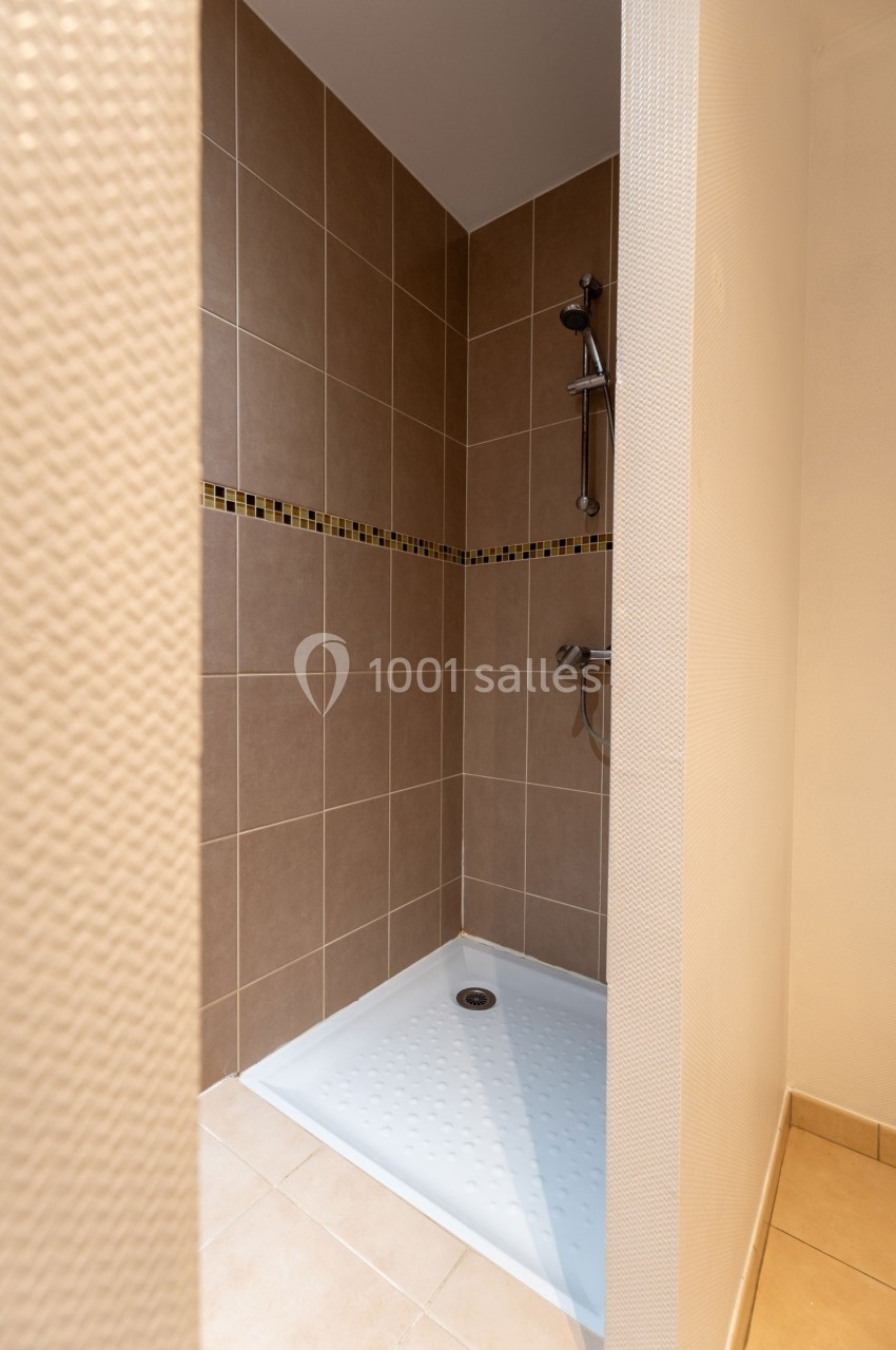 Douche avec carrelage beige et bande décorative, équipée d'une pomme de douche murale et d'un receveur blanc.