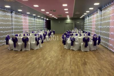 Miniature Location salle Bagnolet (Seine-Saint-Denis) - La Girafe #12 Salle décorée pour un événement avec tables rondes, nappes blanches, chaises ornées de nœuds argentés et dorés, éclairage…