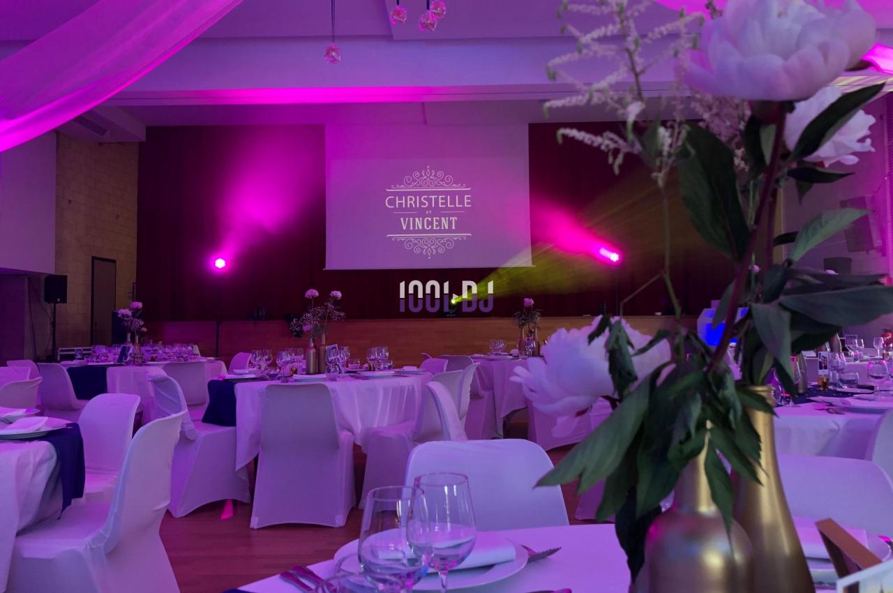 Salle de réception décorée avec des fleurs, éclairage rose et projection lumineuse sur un mur.