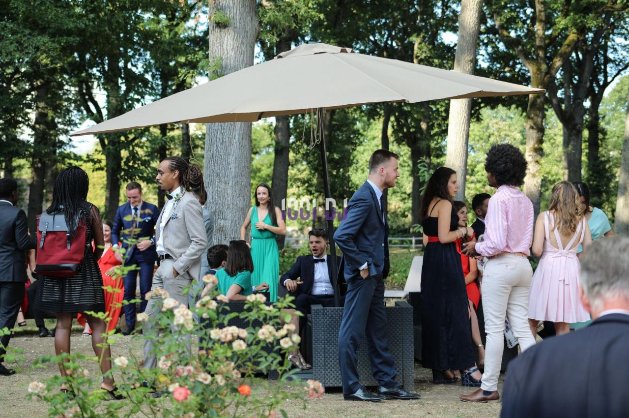 Des personnes discutent et se détendent sous un grand parasol dans un jardin entouré d'arbres et de fleurs.