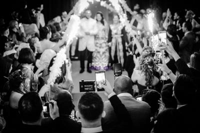 Des mariés avancent sous des étincelles tenues par des invités, entourés d'une foule prenant des photos.