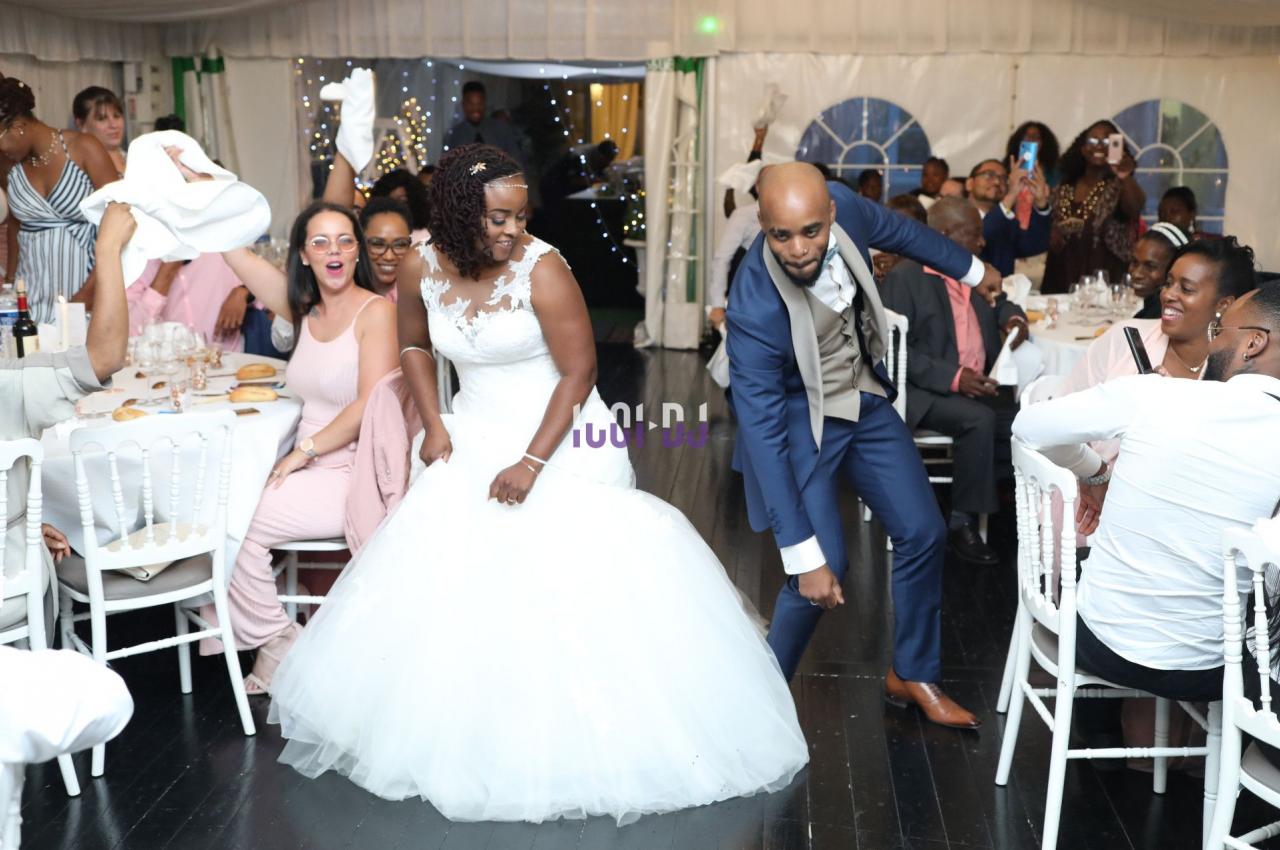Un couple de mariés danse au centre d'une salle festive entourée d'invités applaudissant et souriant.