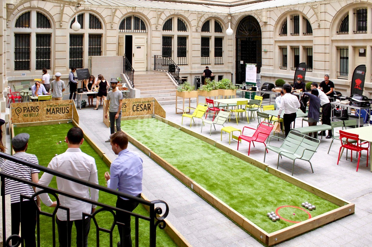 Cour intérieure aménagée avec terrains de pétanque, tables colorées et personnes jouant ou discutant.