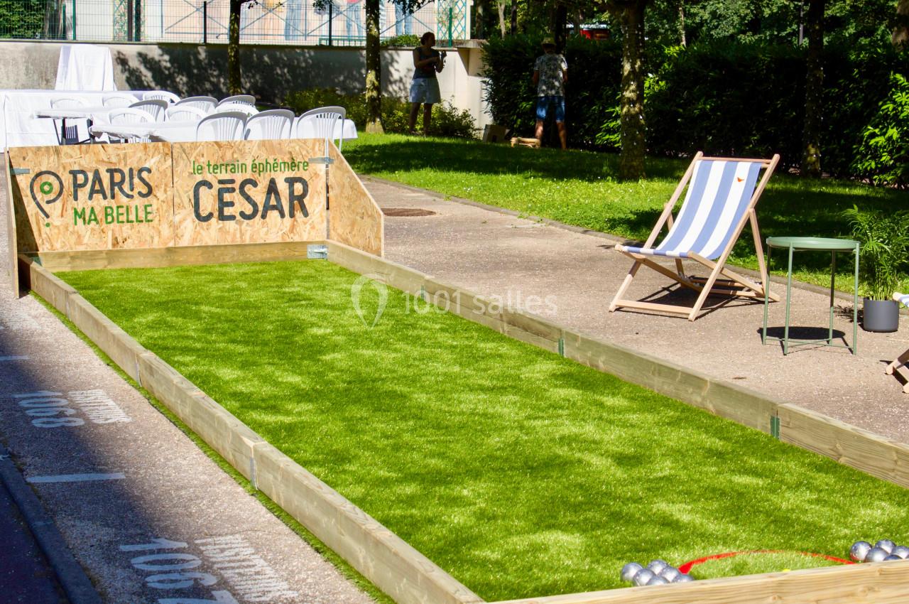 Terrain de pétanque en gazon synthétique avec chaises et parasol, installé dans un espace extérieur ensoleillé.
