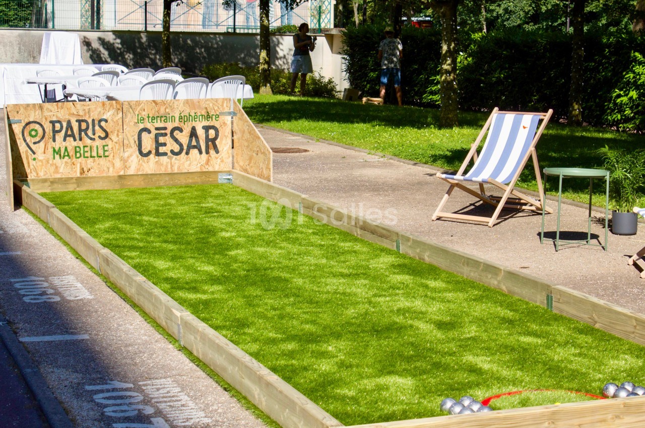 Terrain de pétanque en gazon synthétique avec chaises et parasol, installé dans un espace extérieur ensoleillé.