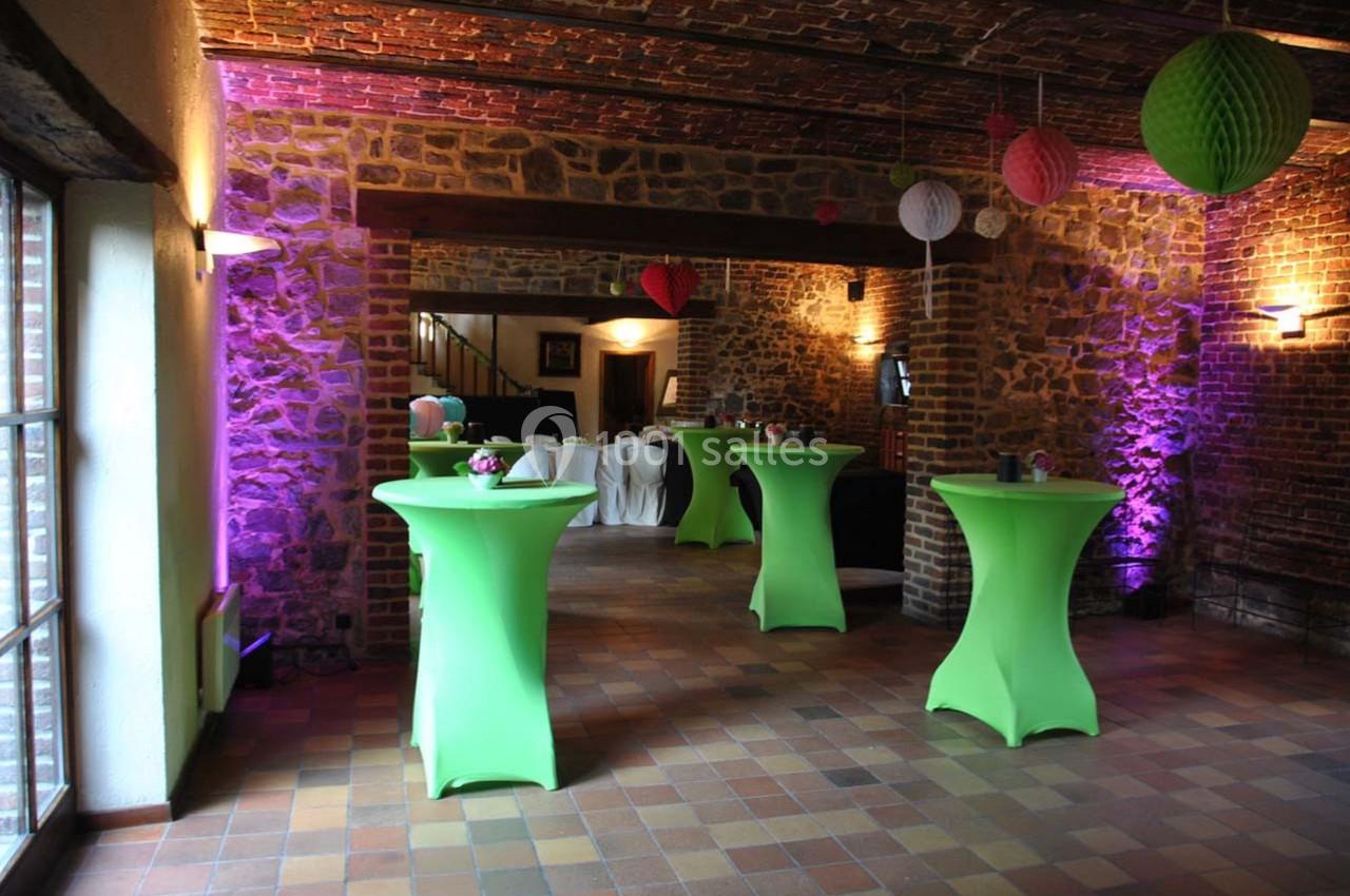 Salle en pierre avec tables hautes vertes, éclairage coloré et décorations suspendues dans une ambiance festive.