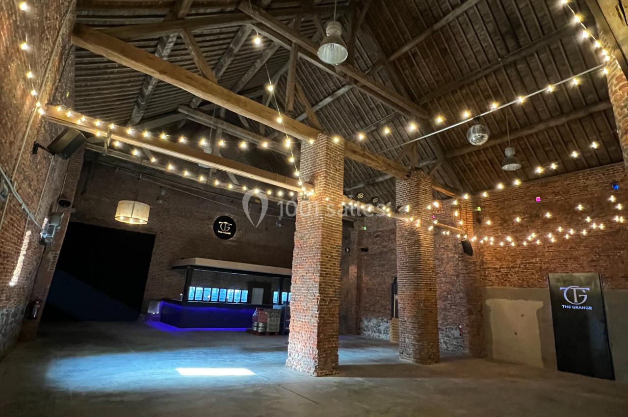 Intérieur d'un bâtiment en briques avec plafond en bois, éclairé par des guirlandes lumineuses suspendues.