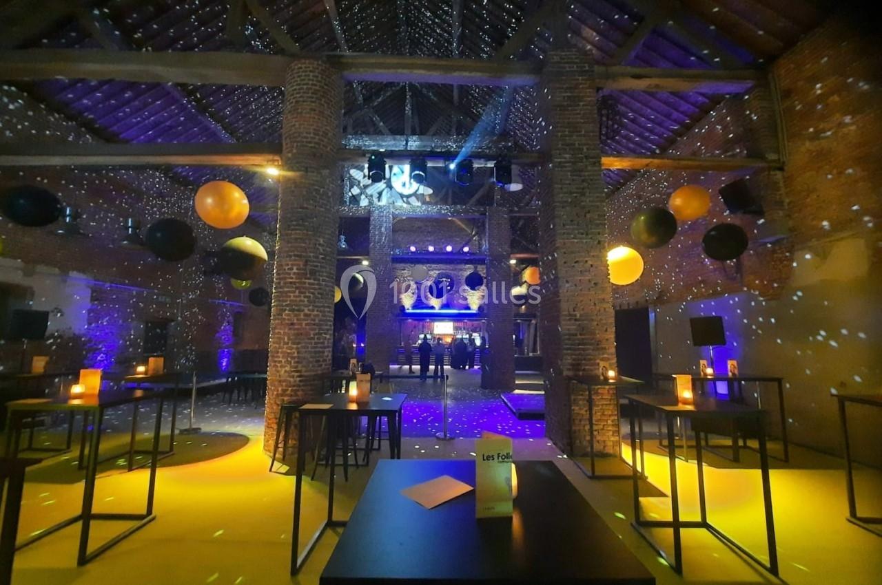 Salle en briques avec tables hautes, éclairages colorés, décorations de ballons noirs et orange, ambiance festive.