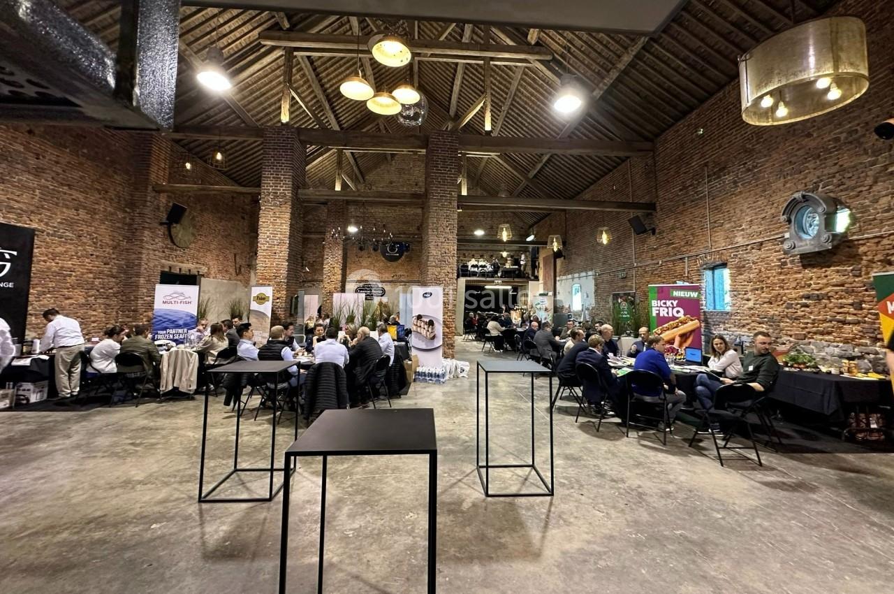 Salle en briques avec des stands d'exposition, des tables et des participants lors d'un événement professionnel.