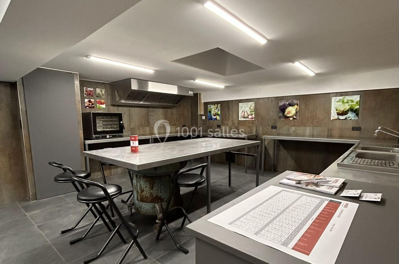 Cuisine professionnelle avec plans de travail en inox, tabourets, four encastré et affiches décoratives au mur.