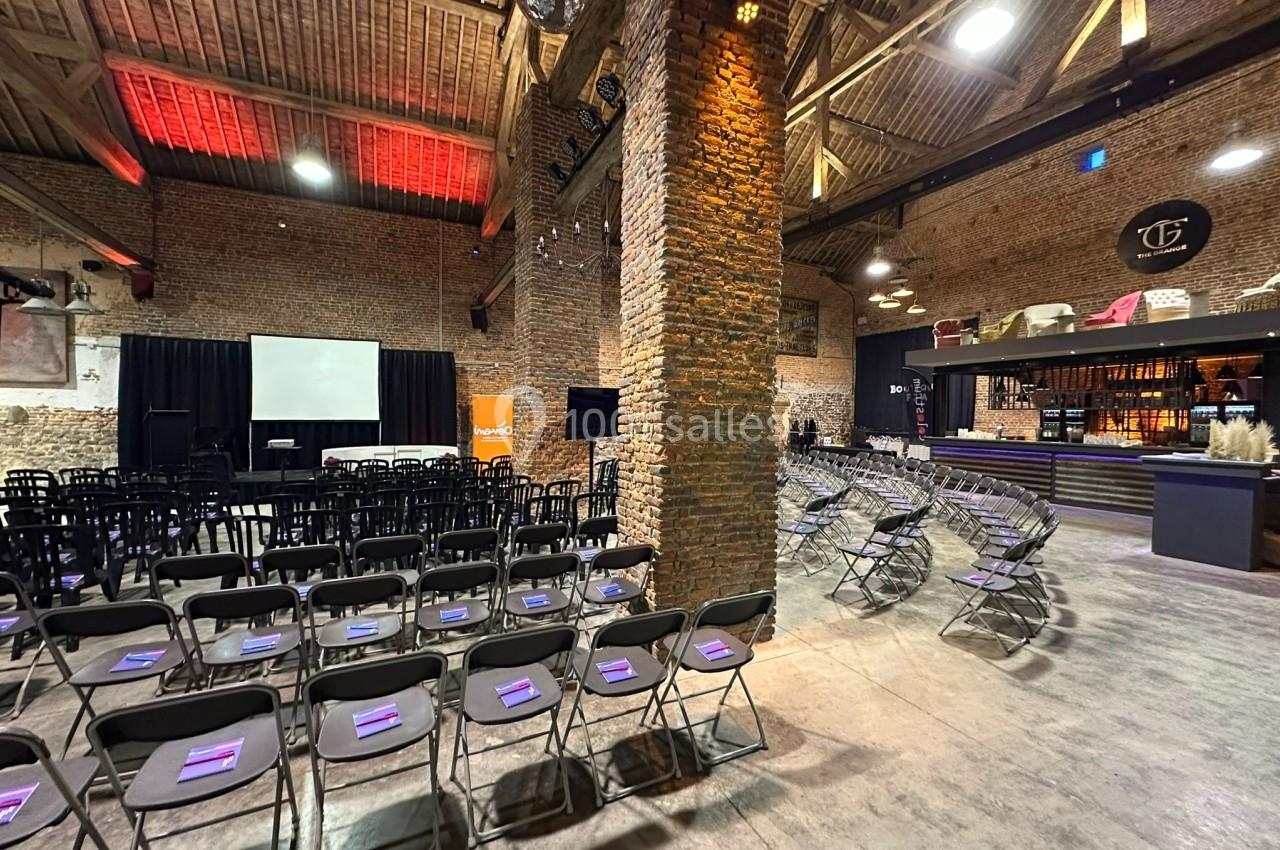 Salle avec des chaises alignées face à un écran de projection, éclairage chaleureux et bar en arrière-plan.
