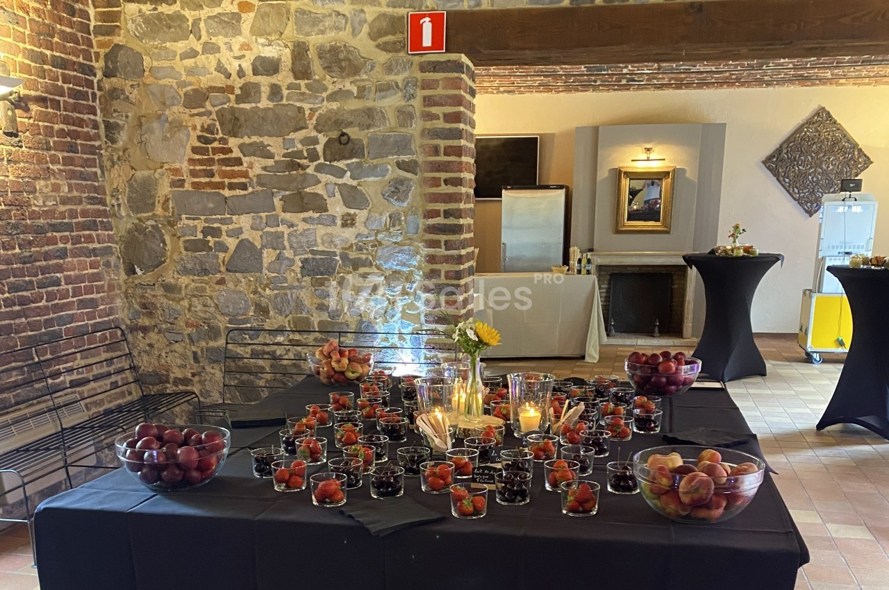 Table décorée avec des bougies, des fruits rouges et des pêches, dans une salle aux murs en pierre et briques apparentes.