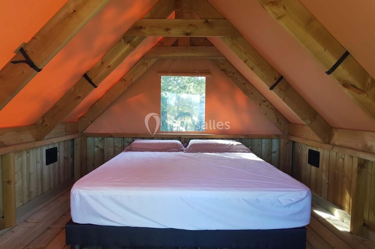 Lit double sous un toit en bois avec une fenêtre laissant entrer la lumière naturelle.