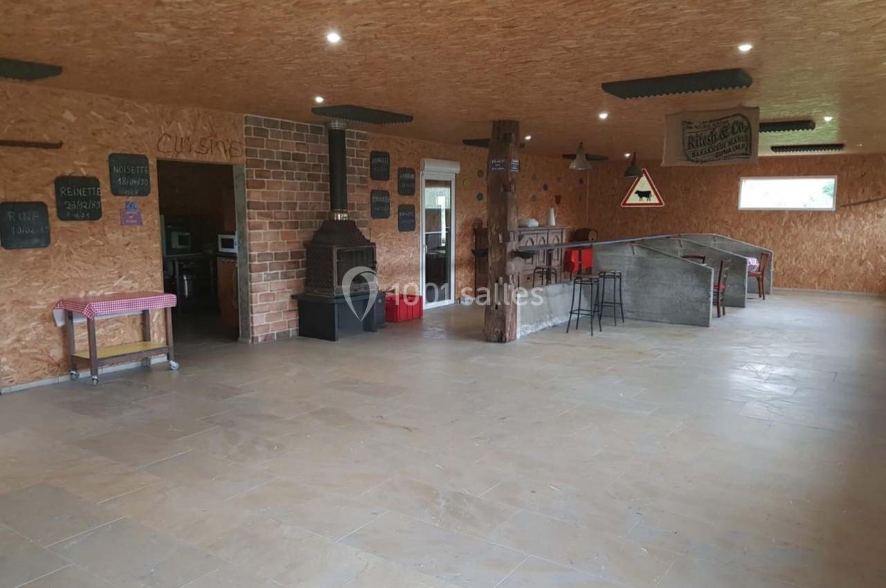 Salle spacieuse avec murs en bois, cheminée en briques, bar en béton et quelques tables et chaises dispersées.