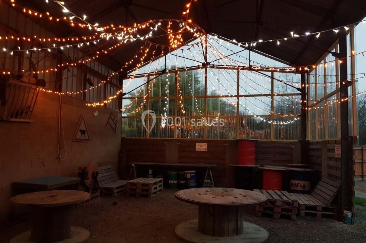 Espace couvert avec guirlandes lumineuses, tables en bois et palettes, ambiance rustique et chaleureuse.