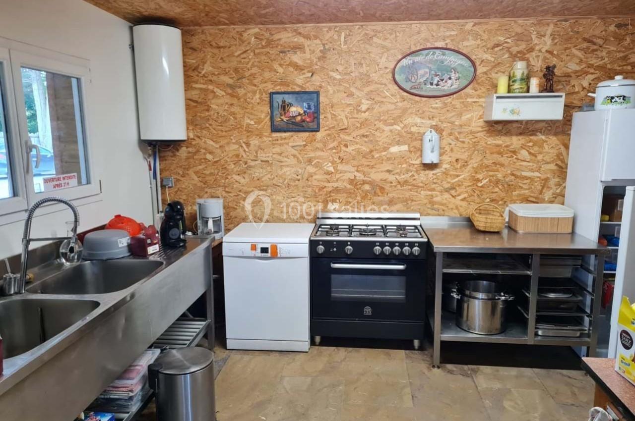 Cuisine équipée avec évier double, lave-vaisselle, cuisinière, plan de travail en inox et mur en panneaux OSB.