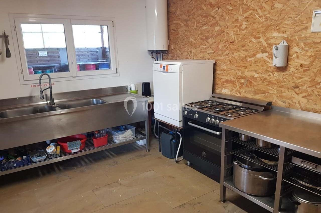 Cuisine simple avec évier inox, cuisinière à gaz, chauffe-eau mural, plan de travail et étagères de rangement.