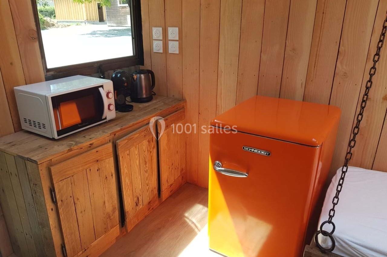 Cuisine en bois avec un réfrigérateur orange, un micro-ondes, une bouilloire et une cafetière sur un plan de travail.