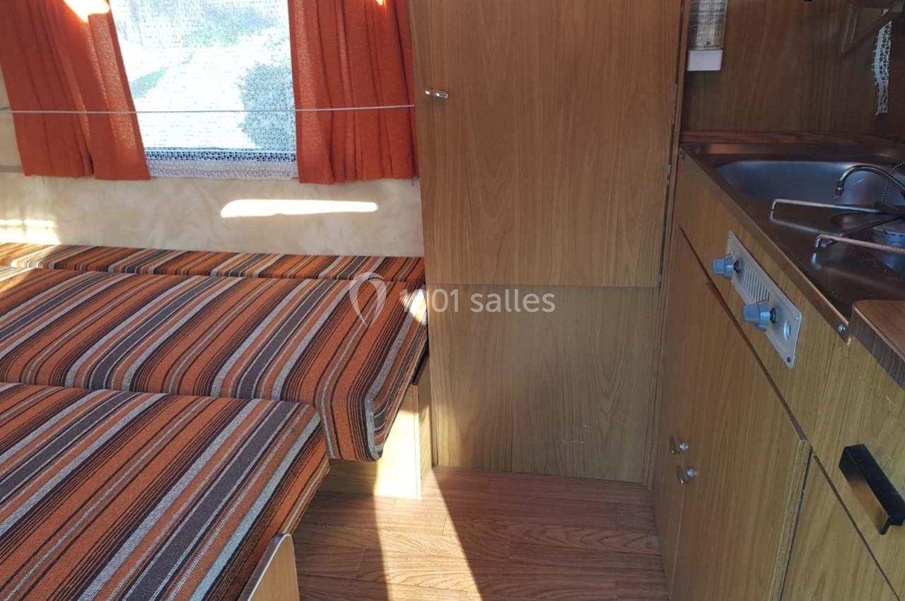 Intérieur d'une caravane avec lits jumeaux à rayures orange, rideaux assortis et coin cuisine en bois clair.