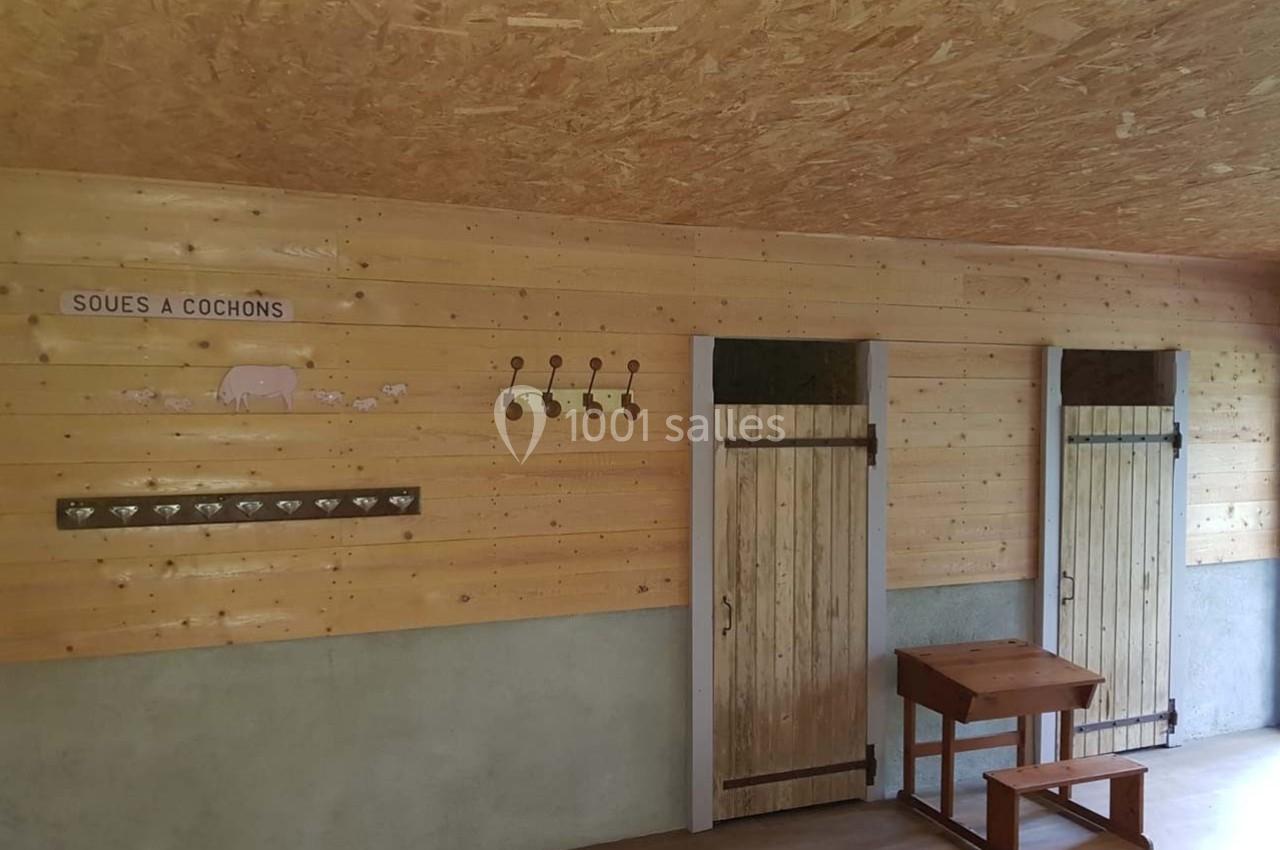 Intérieur d'une porcherie avec murs en bois, portes en bois, crochets muraux et une table en bois.