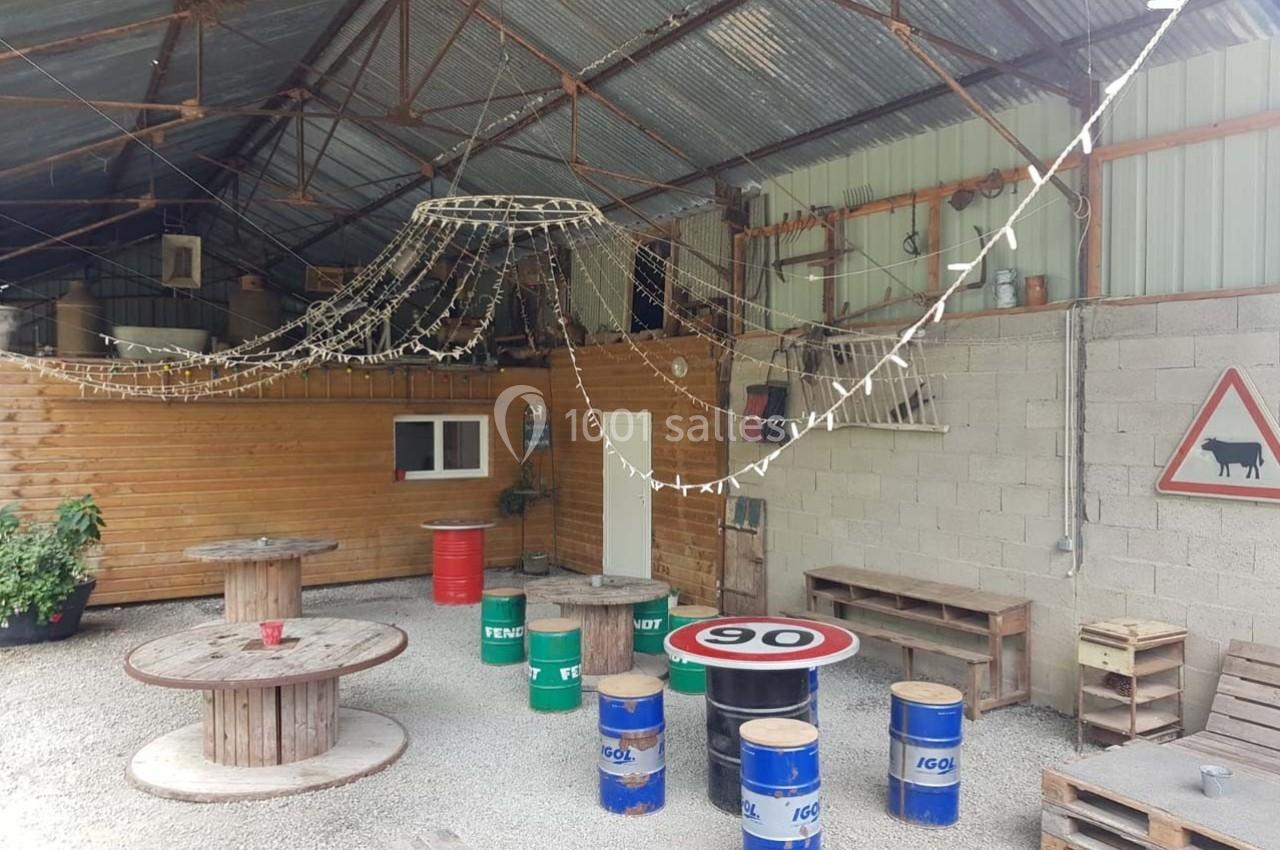 Espace extérieur couvert avec tables en tonneaux, guirlandes lumineuses et décorations rustiques.