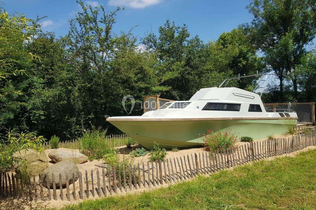 Bateau à moteur hors de l'eau, installé dans un jardin entouré de végétation et d'une clôture en bois.