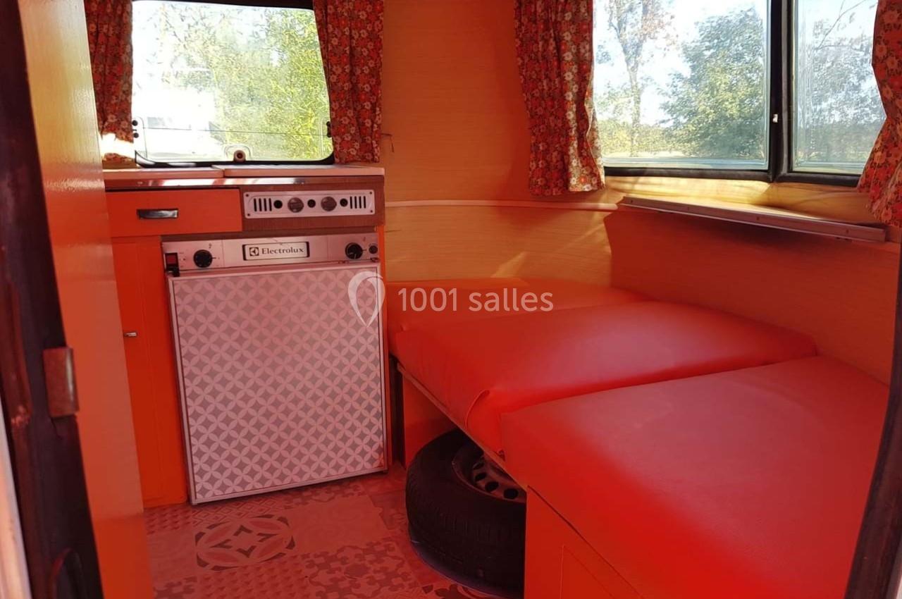 Intérieur d'une caravane rétro avec banquettes rouges, rideaux à motifs et un petit réfrigérateur intégré.