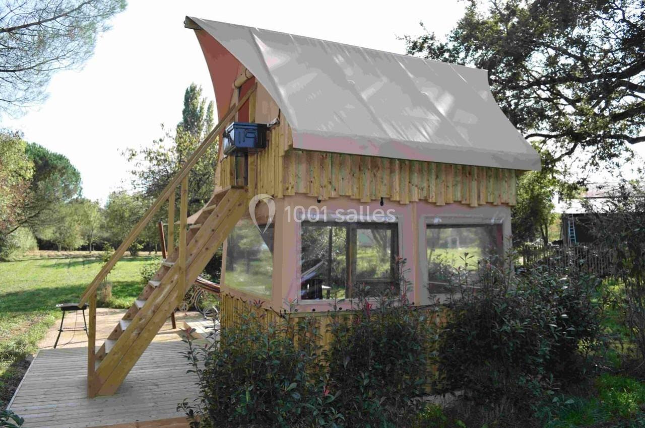 Cabane en bois avec un toit en toile, dotée d'un escalier extérieur et entourée de végétation dans un cadre naturel.