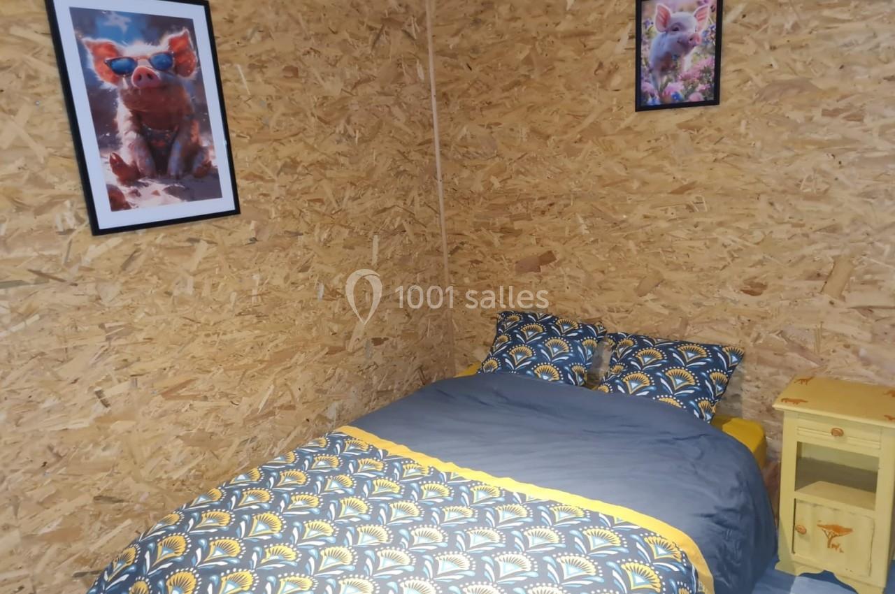 Lit double avec housse de couette à motifs géométriques, dans une chambre aux murs en panneaux OSB décorée de cadres avec…