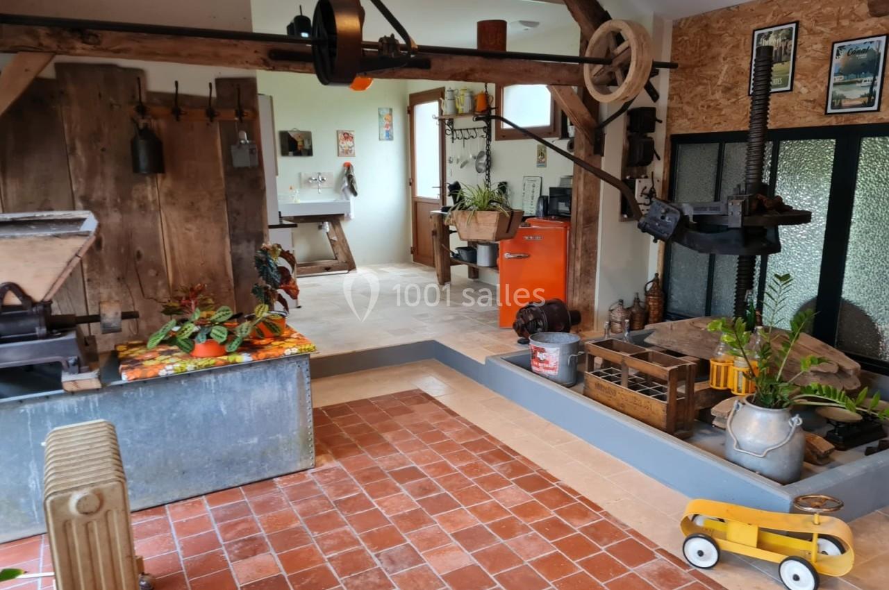 Atelier rustique avec outils anciens, sol en carreaux de terre cuite, jouet en bois et plantes décoratives.