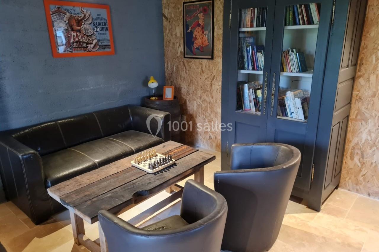 Coin salon avec canapé, fauteuils en cuir, table basse avec jeu d'échecs, bibliothèque et décorations murales.