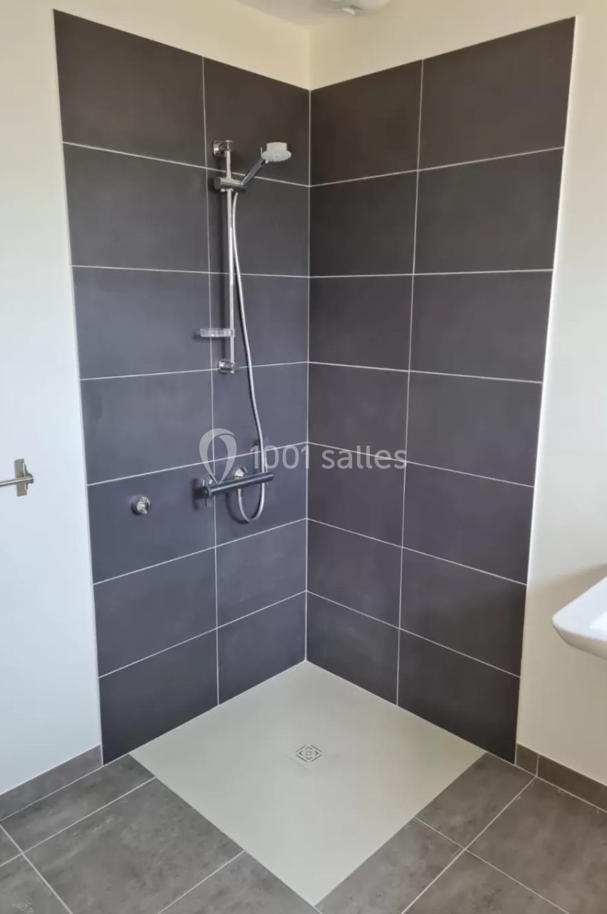Douche à l'italienne avec carrelage gris foncé, receveur blanc et robinetterie murale en acier inoxydable.
