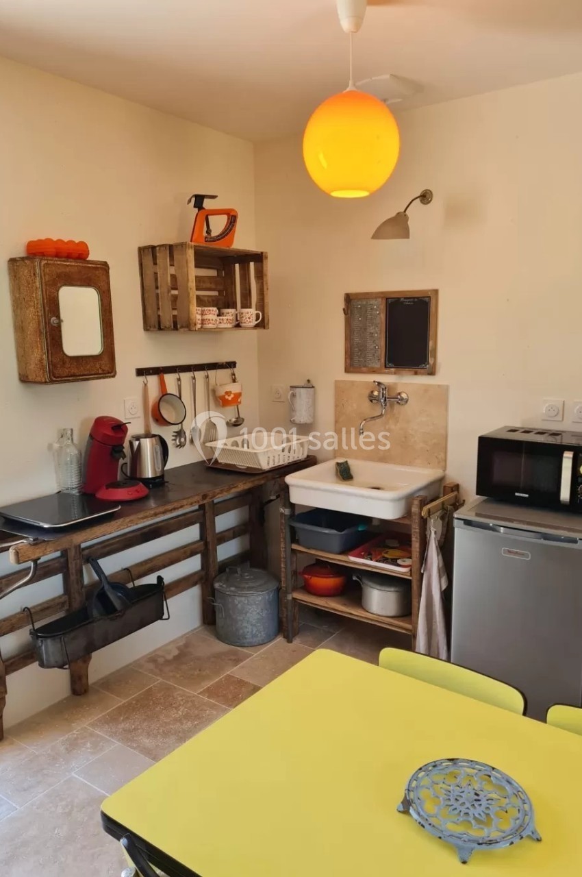 Petite cuisine équipée avec évier, micro-ondes, cafetière, étagères en bois et table jaune.