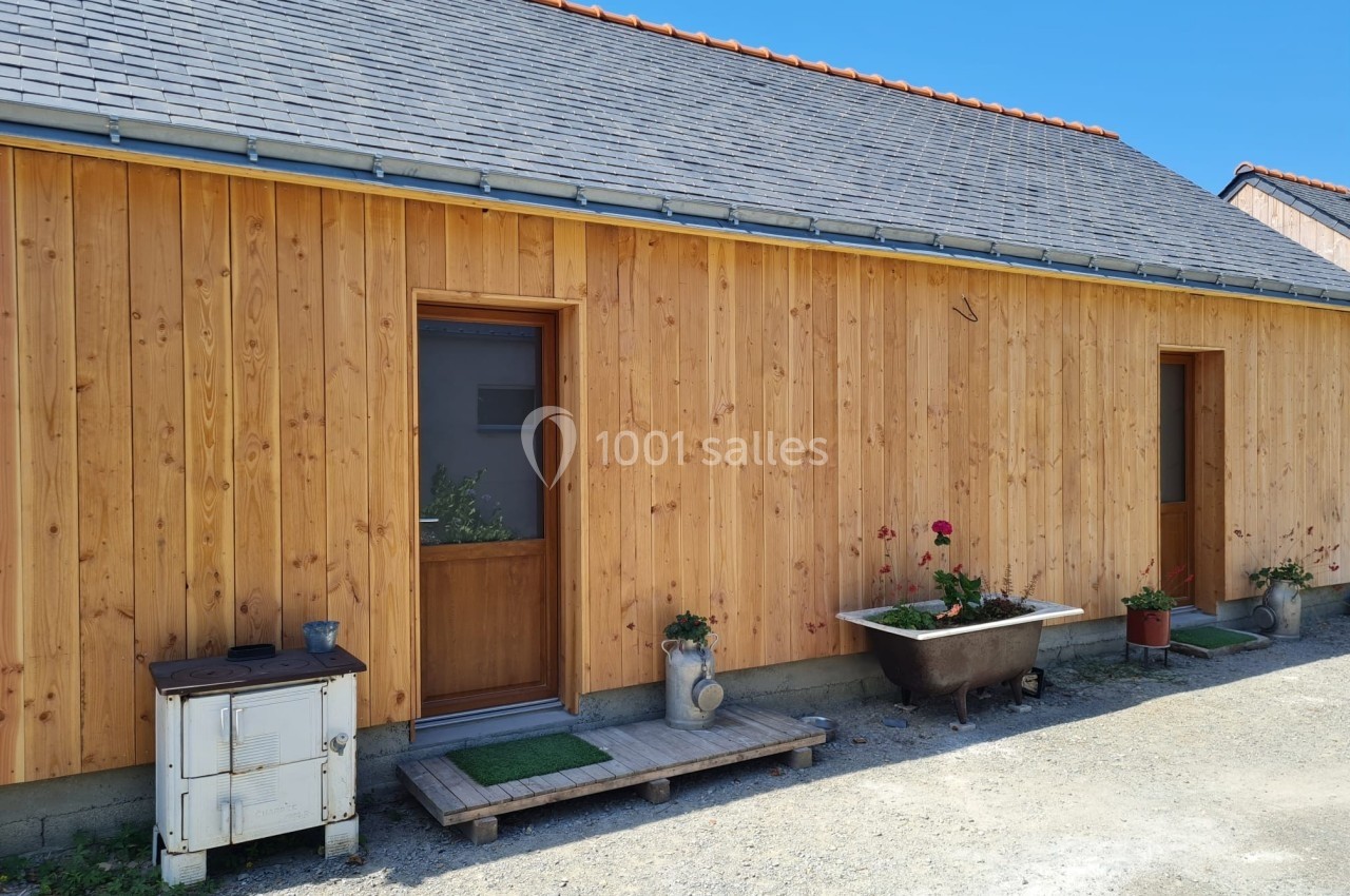 Façade en bois d'une maison avec deux portes, des plantes en pots et une baignoire ancienne en extérieur.