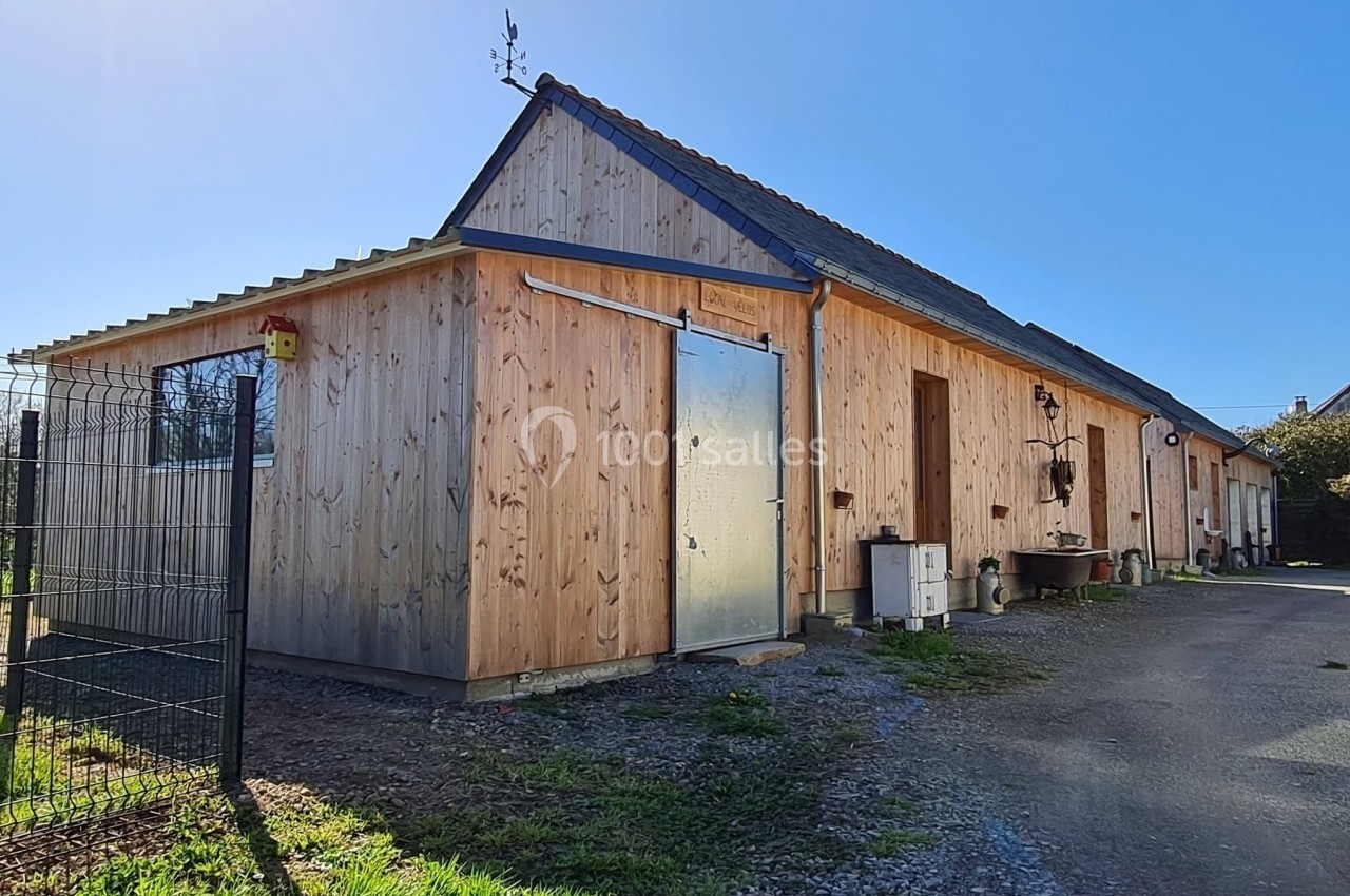 Bâtiment en bois avec toit en pente, porte métallique et clôture grillagée, sous un ciel dégagé.