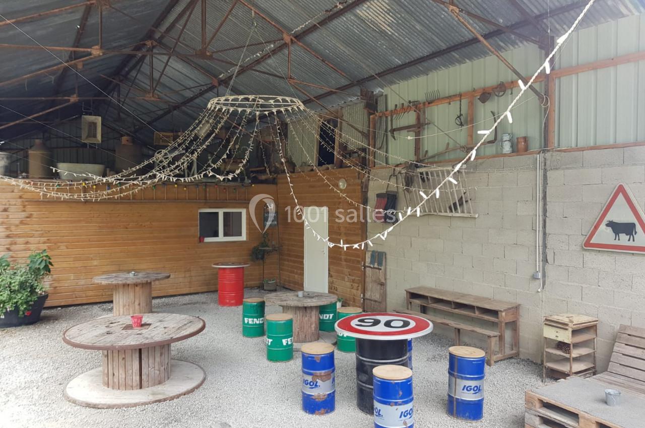 Espace couvert avec tables faites de tonneaux, guirlandes lumineuses suspendues et panneaux décoratifs sur les murs.