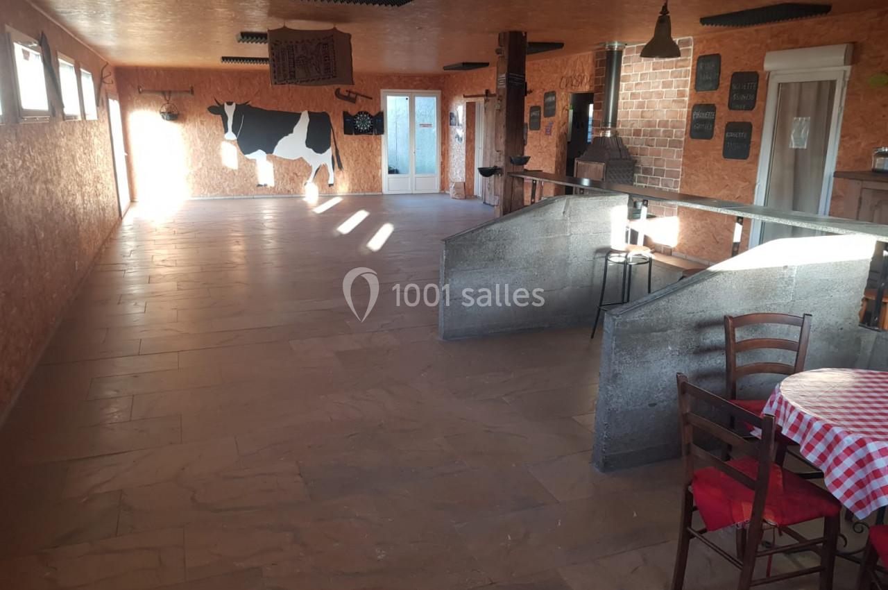 Salle rustique avec murs en bois, décoration murale en forme de vache, table avec nappe à carreaux rouges et chaises.