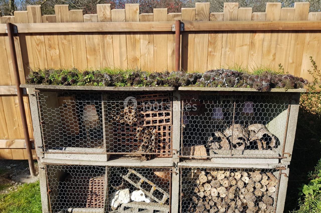 Hôtel à insectes en bois et grillage, rempli de matériaux naturels, installé dans un jardin près d'une clôture en bois.