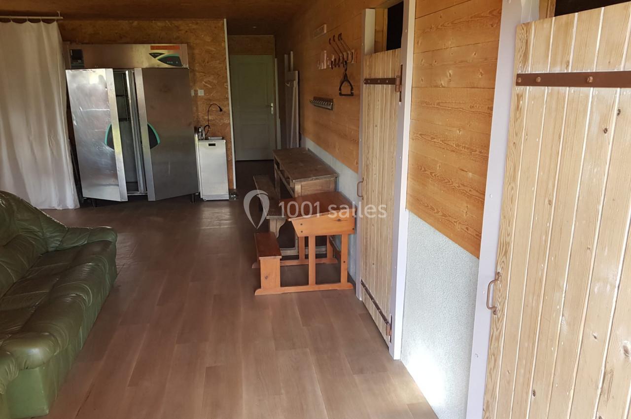 Intérieur d'une pièce avec murs en bois, canapé vert, table en bois, réfrigérateurs et évier au fond.